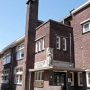 Beetje vertekend beeld van de voorgevel, met entrée en parkeerterrein